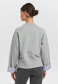 Grå sweatshirt med rund halsringning, raglanärmar och randiga mudd. Mjuk textur med kontrasterande blå och vit randig tyg vid ärmarnas slut.