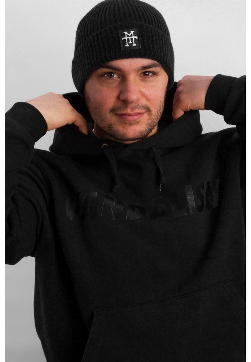 Black hoodie with "VANDALISK" in embossed text, styled with a ribbed black knit beanie featuring white logo, worn by a person pulling the hoodie.