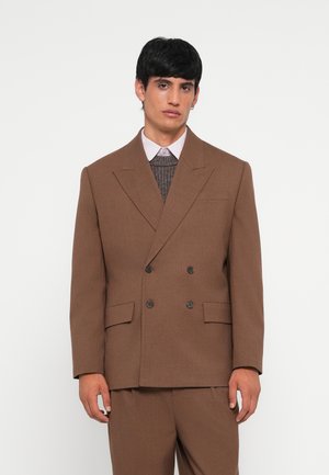 Brown double-breasted blazer made of textured fabric, featuring notched lapels, two front pockets, and black buttons, paired with a knit sweater.