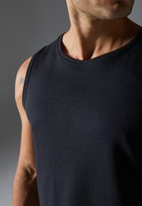 Men’s black sleeveless shirt made of soft cotton, featuring a round neckline and smooth texture, with detailed stitching around the armhole.