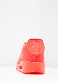 Tenisky Nike Air v jasně červené barvě, vyrobené z texturovaného materiálu, s polstrovaným límcem a logem na patě. Design doplňuje pevná gumová podrážka.