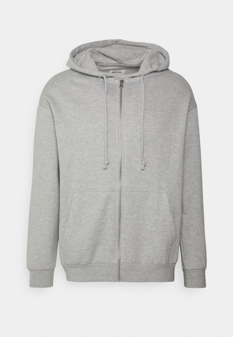 Sweat à capuche gris clair zippé avec cordon et poches avant, présenté sur un fond clair uni.