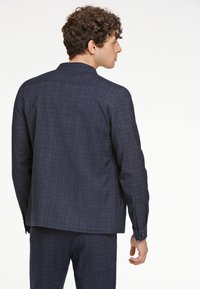 Marinblå rutigt blazer, tillverkat av texturerad tyg. Anm ärkningsvärda detaljer inkluderar en skräddarsydd passform, subtilt rutmönster och knapppärlor vid ärmsluten.