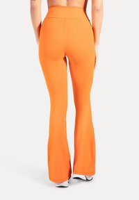 Liehuvat legginssit kirkkaassa oranssissa värissä. Valmistettu sileästä, joustavasta kankaasta, jossa on korkea vyötärönauha. Yksinkertainen muotoilu, ilman näkyviä kuvioita tai korostuksia.