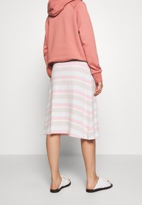 Randig kjol i ljusrosa, blå och beige bomull med en utfläkt design, matchad med en korallfärgad hoodie och vita sandaler.