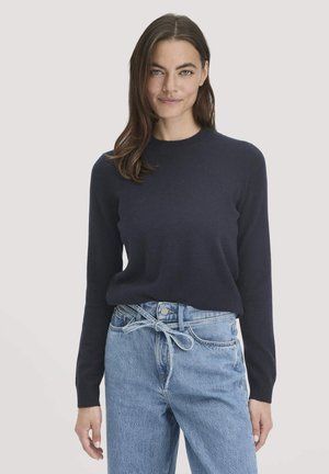 Navyblauer Pullover mit langen Ärmeln aus einem strukturierten Strickstoff, getragen mit hochgeschnittenen hellblauen Jeans aus Denim mit einem gebundenen Gürtel-Detail.