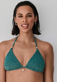 Tyrkysový textúrovaný trojuholníkový bikiny top s nastaviteľnými popruhmi a zlatou mušľou v strede. Hladká, elastická tkanina.