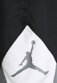 Pantalones cortos deportivos negros con tela texturizada; cuentan con un panel triangular blanco con una silueta gris del logotipo de Jordan.