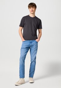 Camiseta de manga corta gris oscuro, escote redondeado, sutil logo en el pecho, combinada con jeans rectos de tono azul claro y zapatillas altas beige.