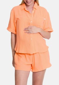 Leichter, orangefarbener zweiteiliger Schlafanzug bestehend aus einem kurzärmeligen, knöpfbaren Hemd mit Tasche und lockeren Shorts. Strukturierter Stoff.
