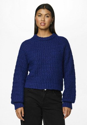 Maglione azzurro lavorato a maglia con un motivo testurizzato, colletto rotondo e maniche lunghe, abbinato a pantaloni neri. Il materiale appare spesso e caldo.