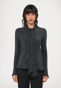 Dunkelgraue Bluse mit einem Bindungsdetail am Hals, langen Ärmeln und einem glatten, fließenden Stoff, der sanft über den Körper fällt.