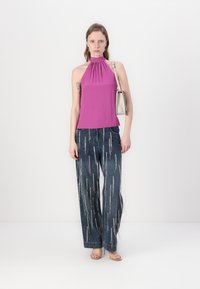 Fialová halter top s zhromaždeným výstrihom, v kombinácii s širokými rifľovými nohavicami s vertikálnymi svetlými pruhmi a svetlými sandálmi.
