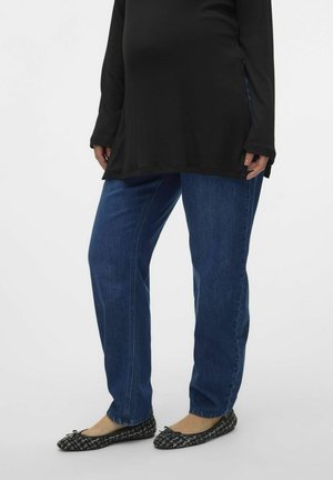 Haut noir à manches longues avec fentes sur les côtés, associé à un jean droit bleu et des ballerines noires à motifs. Tenue décontractée avec des tons neutres.