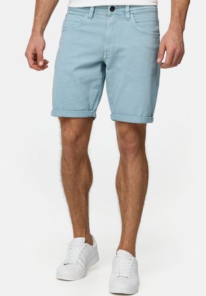 Shorts en denim bleu clair avec un revers, dotés de poches avant et d'une fermeture à bouton. Portés avec des baskets blanches.