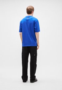 Μπλε κοντομάνικο μπλουζάκι με στρογγυλή λαιμόκοψη, με ετικέτα λογότυπου στο πίσω μέρος. Συνδυάζεται με φαρδιά μαύρα παντελόνια cargo.