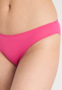 Rosa bikinitruse med en glatt, elastisk tekstur. Har delikat søm langs kantene, designet for komfort og passform.