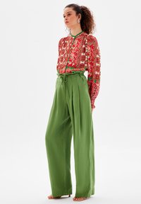 Röd mönstrad blus med gröna detaljer, försedd med kn�äppning framtill och plisserade gröna högmidjade byxor. Eleganta sandaler fulländar looken.