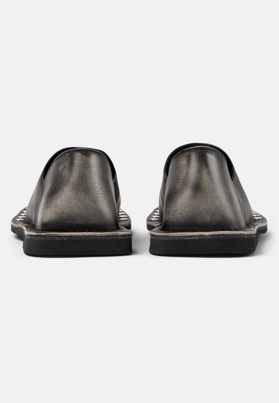 Paire de chaussures en cuir noir sans lacets vue de dos, montrant des semelles plates et des panneaux de talon lisses sur un fond blanc.