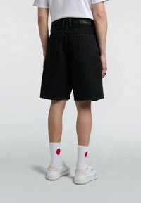Shorts di denim neri con una vestibilità rilassata, vita media e tasche posteriori. Abbinati a sneakers bianche e calzini bianchi con un punto rosso.