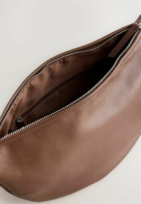 Braune Lederhandtasche mit glatter Oberfläche, runder Form und Reißverschluss oben. Das Innere hat eine dunkle Fütterung und eine Reißverschlusstasche.