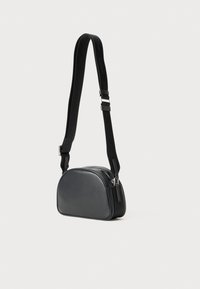 Čierna kožená crossbody taška s okrúhlym tvarom, so zipsovým uzatvorením a nastaviteľným popruhom s embosovaným logom.