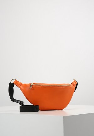 Oranje leren taille tas met gouden rits en verstelbare zwarte riem, liggend op een witte ondergrond tegen een effen achtergrond.