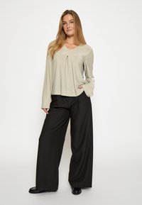 Gara piedurkņu, gaiši zaļa blūze ar V veida izgriezumu, ar priekšējo krokas dizainu, kombinēta ar brīvām melnām biksēm un spīdīgām melnām kurpēm.