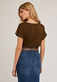 Brun kortärmad topp med rullade ärmar, som kombineras med en blå denimkjol med bakfickor och ett brunt bälte. Slät textur, avslappnad passform.