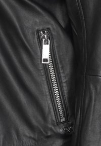 Sort læderjakke med en glat tekstur, sølvfarvet lynlåslomme og et diskret brandingdetalje nær kanten.
