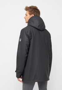 Giacca nera impermeabile con cappuccio, caratterizzata da un logo sulla manica e da un esterno liscio e lucido. Il design è di vestibilità comoda.