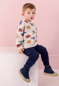 Sweatshirt gris clair avec des imprimés de dinosaures colorés, associé à un pantalon cargo marine et des baskets montantes bleu foncé avec des semelles beiges.