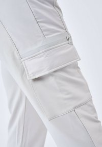 Lichtgrijze cargobroek met rits- en klepzakken. Glad, lichtgewicht stof met een matte afwerking en subtiele stikseldetails.