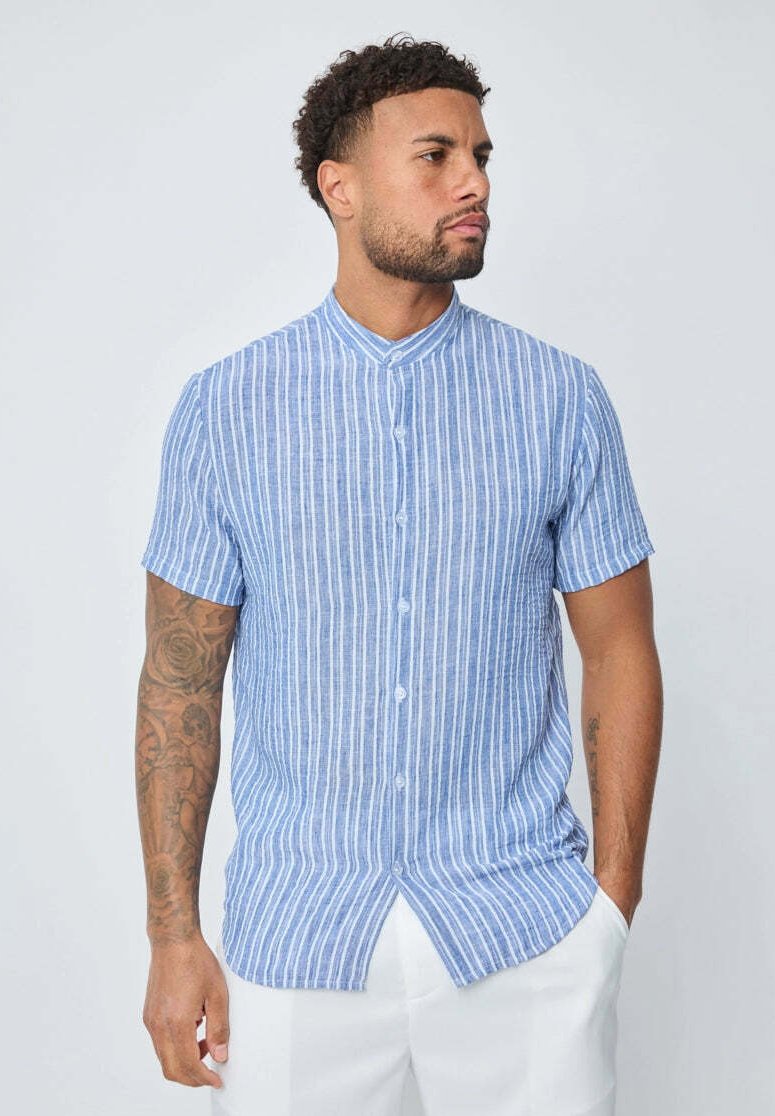 Chemise à manches courtes bleue et blanche à rayures, avec un col montant, fabriquée dans un tissu léger et dotée d'une coupe droite avec des fentes latérales.