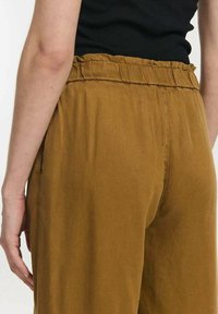 Mosterdgele wijde broek met een elastische tailleband en zijzakken, gemaakt van een zachte, lichte stof. Smooth textuur, casual design.