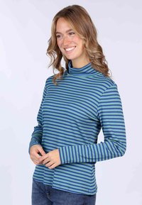 Langärmliges Turtleneck-Shirt in Blau- und Grüntönen mit gerippter Textur und lockerer Passform, kombiniert mit Jeans.