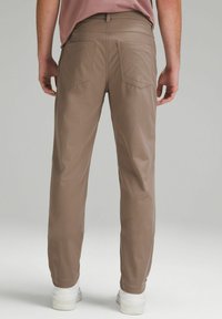 Ruske, skræddersyede bukser lavet af glat stof. Har to baglommer med en sømløs design og lige ben, parret med hvide sneakers.