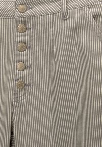 Striped fabric with gray and cream colors, featuring five large metal buttons and visible stitching details at the waistline and pockets.
