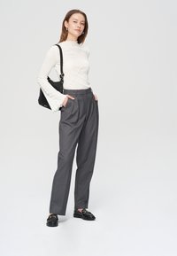 Biały, ryflem zdobiony top z długim rękawem z falbaniastymi mankietami, połączony z taliowanymi, szarymi spodniami o wysokim stanem i czarnymi mokasynami oraz czarną torebką.