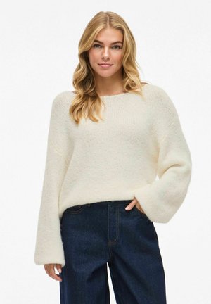 Pullover di maglia di colore crema, oversize, con vestibilità ampia e maniche larghe. Presenta una texture morbida, scollatura rotonda e uno stile casual.