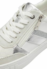 Sneaker bianco con accenti metallici argento, design con lacci, texture perforata, chiusura laterale con zip e una suola spessa bianca.