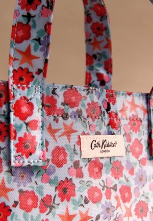 Detailní záběr na látkovou tašku s květinovým vzorem, obsahující červené, růžové a fialové květiny a hvězdicové tvary, s přišitou štítkem "Cath Kidston London".