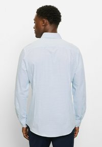 Blaues Hemd mit Knopfleiste und kleinem marineblauem Polka-Dot-Muster. Mit Kragen, langen Ärmeln und abgerundetem Saum. Hergestellt aus glattem Stoff.