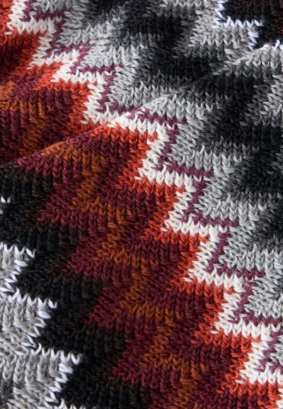 Gros plan d'un tissu tricoté avec des motifs en zigzag gris, noir, blanc, bordeaux, orange et marron.