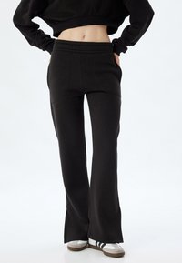 Zwarte sweatpants met een uitlopende pasvorm, voorzien van een elastische tailleband en zijzakken, gemaakt van zacht materiaal met een gladde textuur.