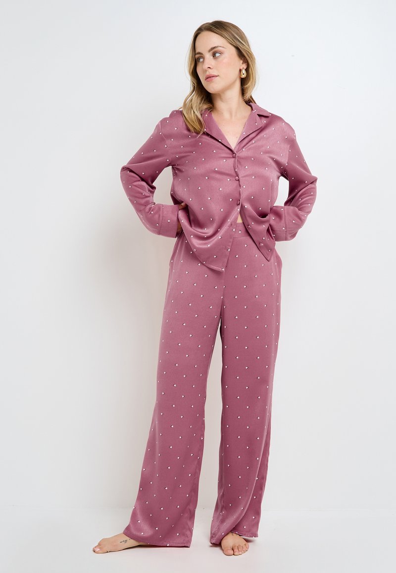 Ensemble de pyjama à manches longues, avec boutons, en mauve, présentant de petits motifs de cœurs blancs, coupe décontractée et texture douce. Le pantalon possède une taille élastique.