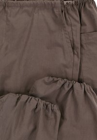 Bruine broek met elastische tailleband van een gladde, lichte stof. Voorzien van geplooide details bij de enkels enzij pockets voor functionaliteit.