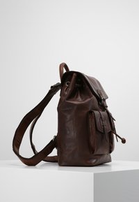Brun läderryggsäck med en strukturerad form, med dragsko-stängning, framfickans lock och justerbar axelrem.