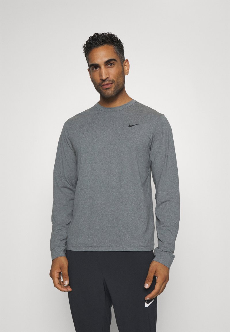Hosszú ujjú szürke Nike póló, amely kerek nyakkivágással és egy kis fekete logóval rendelkezik a bal melle fölött. Simább, sportos szabású anyag.