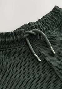 Mörkgröna mesh-fabric shorts med elastisk midja och dragsnodd med metallaglets. Texturerad yta med en andningsbar design.
